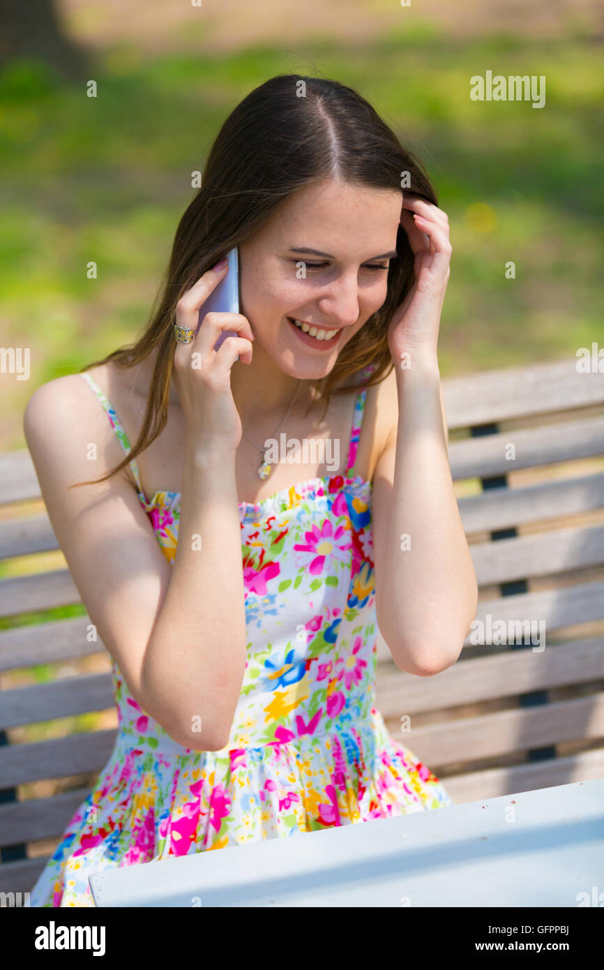Una ragazza che indossa abiti di colore usato il cellulare in estate park Foto Stock