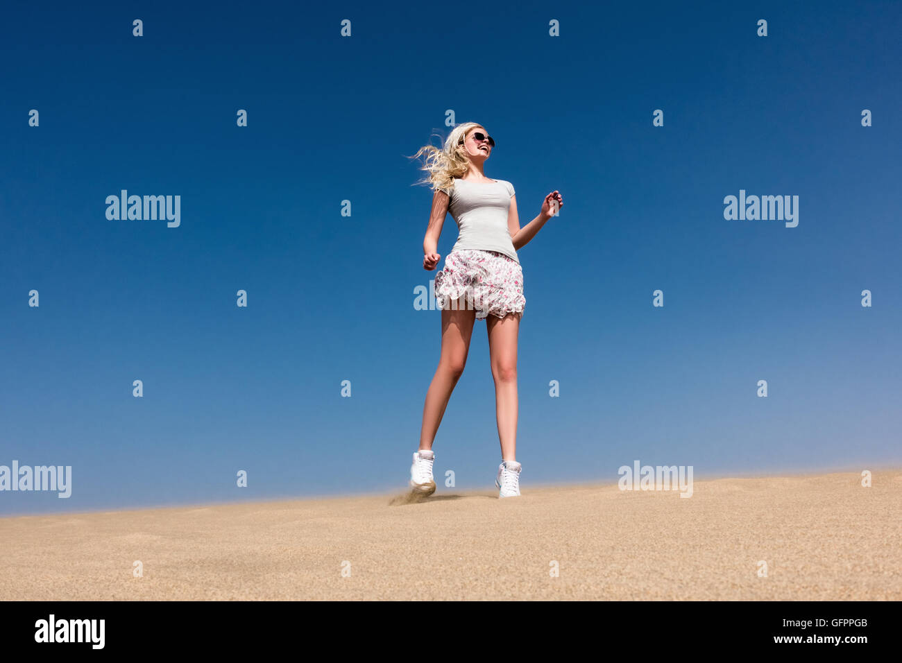 Una giovane ragazza che indossa un mantello di saltare sul deserto di sabbia Foto Stock