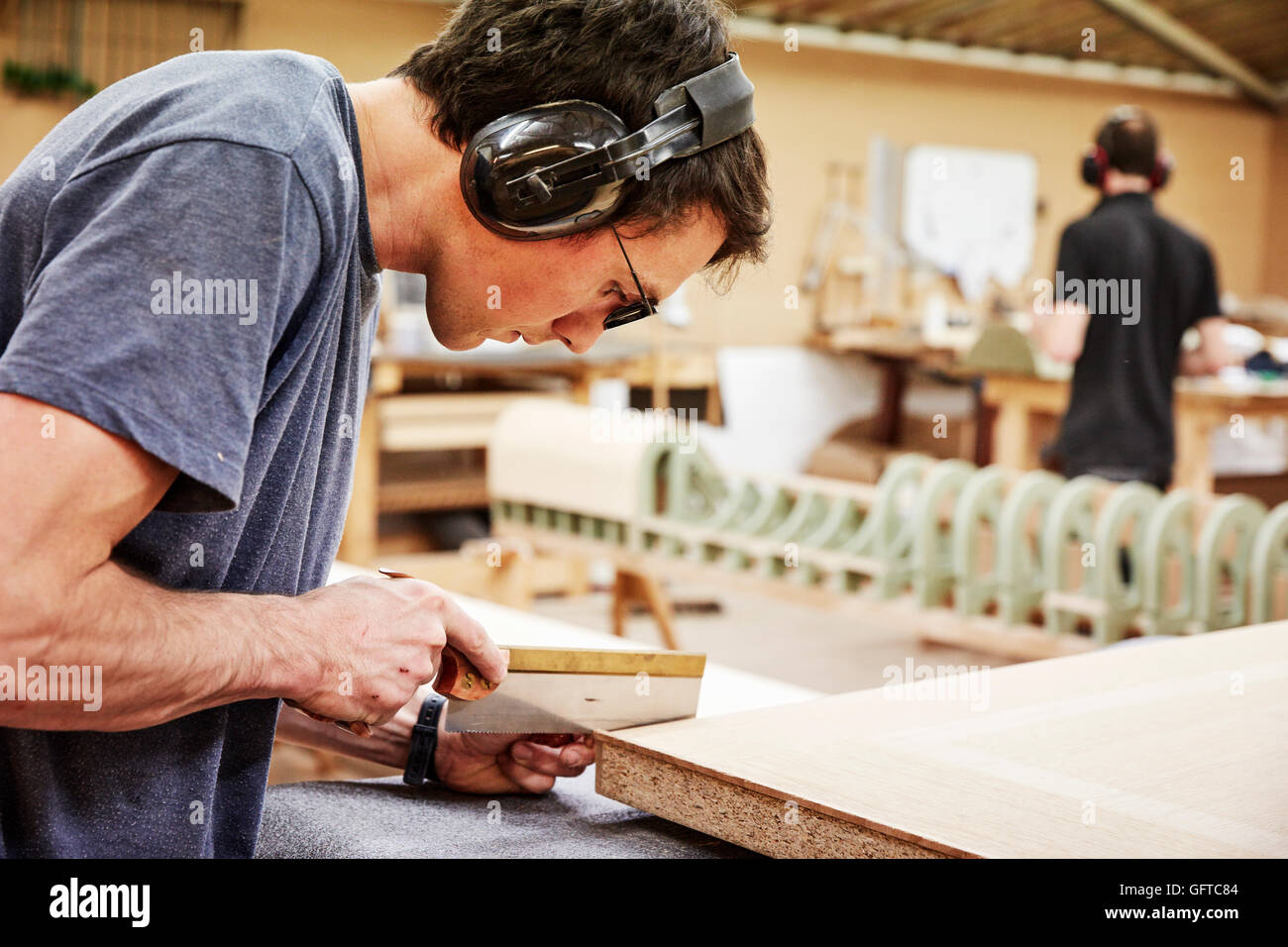 Un workshop di mobili ,un uomo con un piccolo handsaw per tagliare il legno Foto Stock