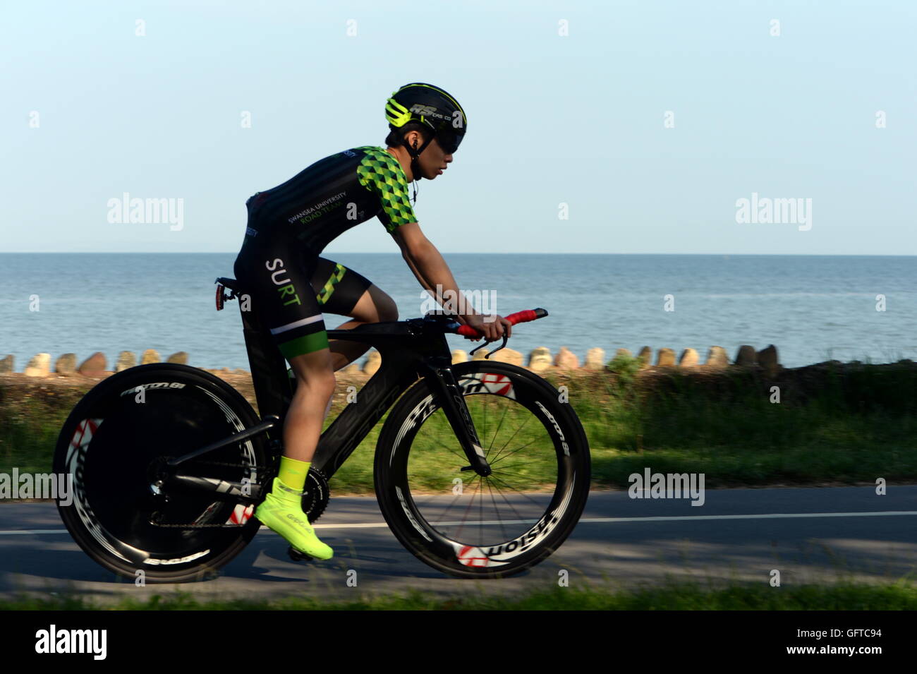 Ciclista di velocità sulla costa della Baia di Swansea. Pezzata ombra e luce del sole serale aggiungere al godimento della corsa. Foto Stock