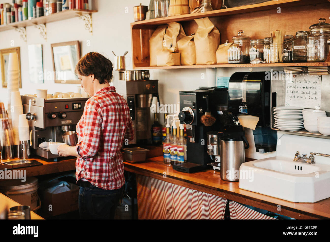 Una donna in un plaid shirt lavorare dietro il bancone in un coffee shop Foto Stock