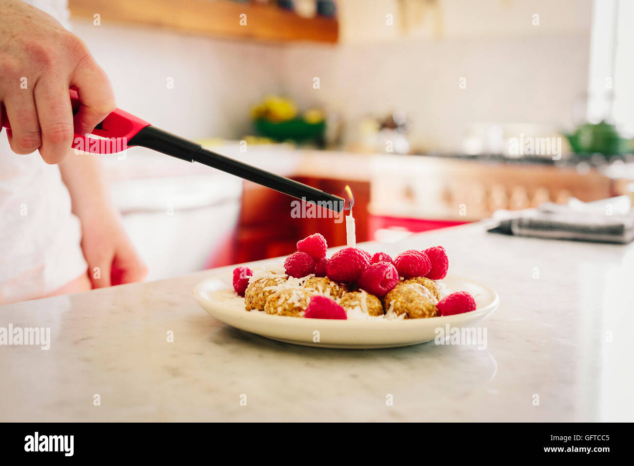 Una piastra con un dessert e lamponi freschi e una mano che regge un accendino per la candela Foto Stock
