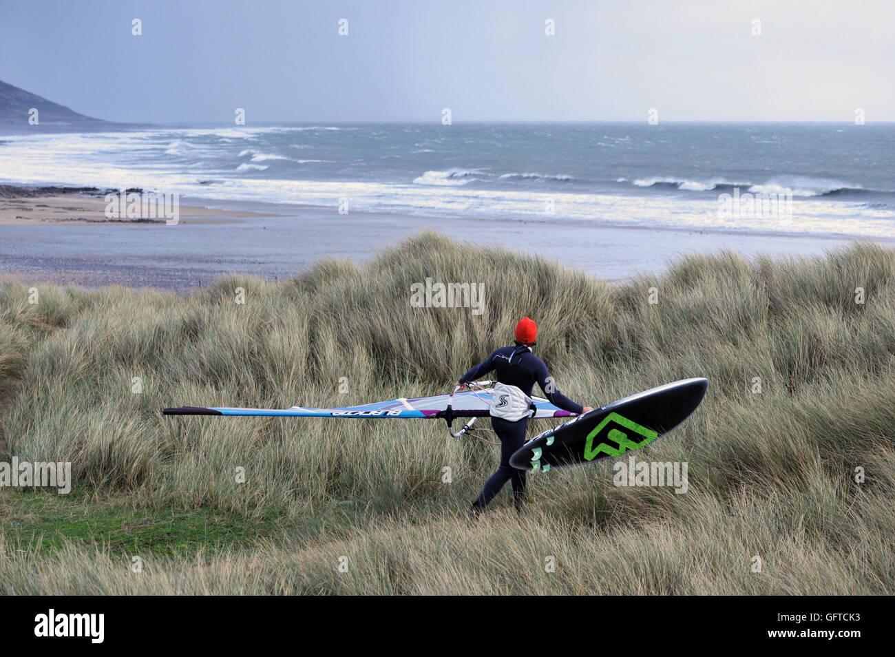 Windsurf controlla le condizioni di surf come egli cammina oltre le dune della spiaggia a Port Eynon, Gower, Galles Foto Stock