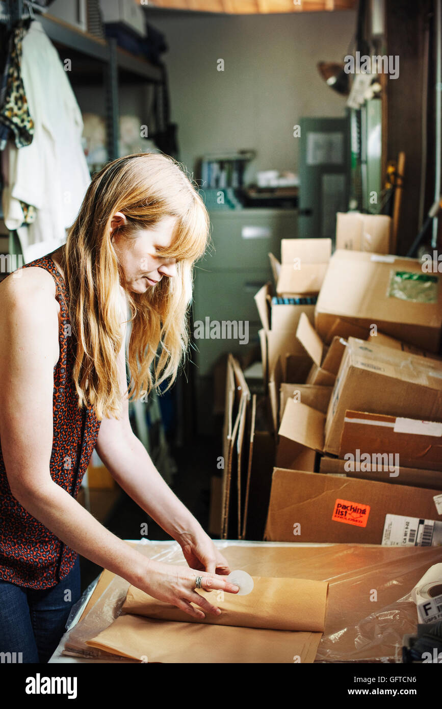 Donna con capelli lunghi biondi in piedi nel magazzino di un negozio di merchandising di incarto in carta marrone Foto Stock