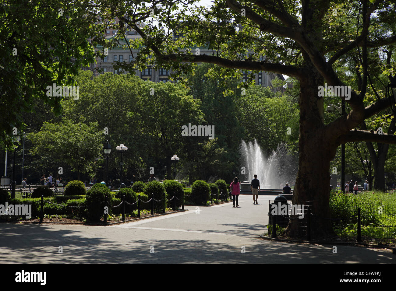 La gente camminare nei pressi della fontana di Washington Square Park di New York, sotto gli alberi Foto Stock