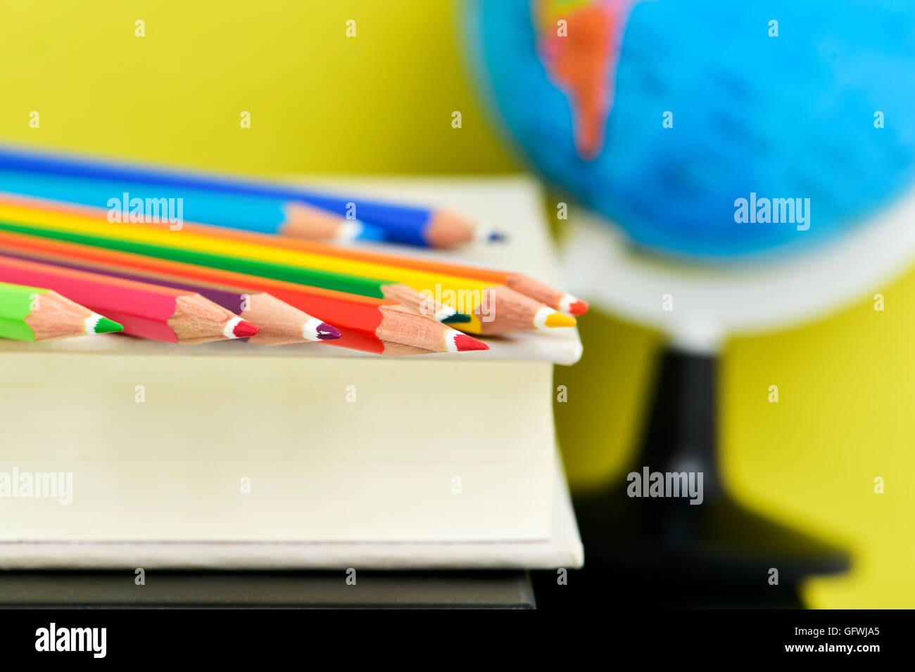 Primo piano di una pila di matite di diversi colori su una pila di libri e un globo terrestre in background, contro un Foto Stock