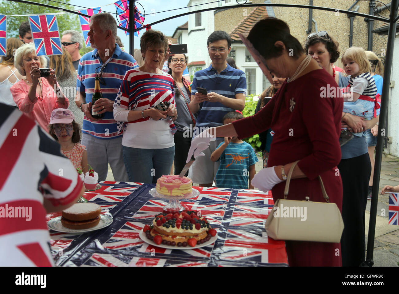 Street partito svoltasi nella celebrazione della Regina Elisabetta II il novantesimo compleanno - donna che indossa una maschera e vestita come la regina tagliare la torta con la gente a guardare la Cornovaglia Road Surrey in Inghilterra Foto Stock