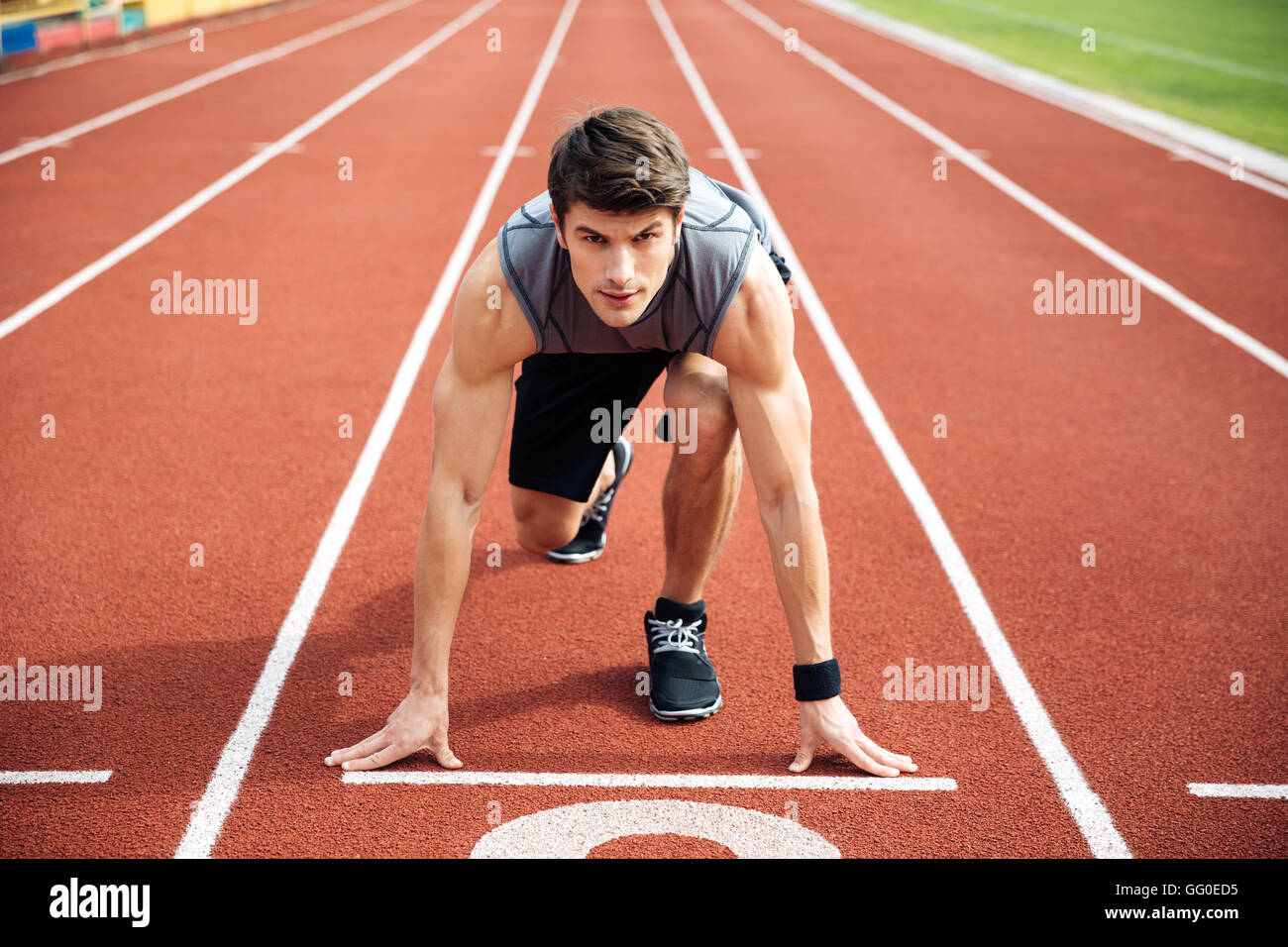 Ritratto di giovane muscolare atleta concentrato all'inizio del tapis roulant presso lo stadio Foto Stock