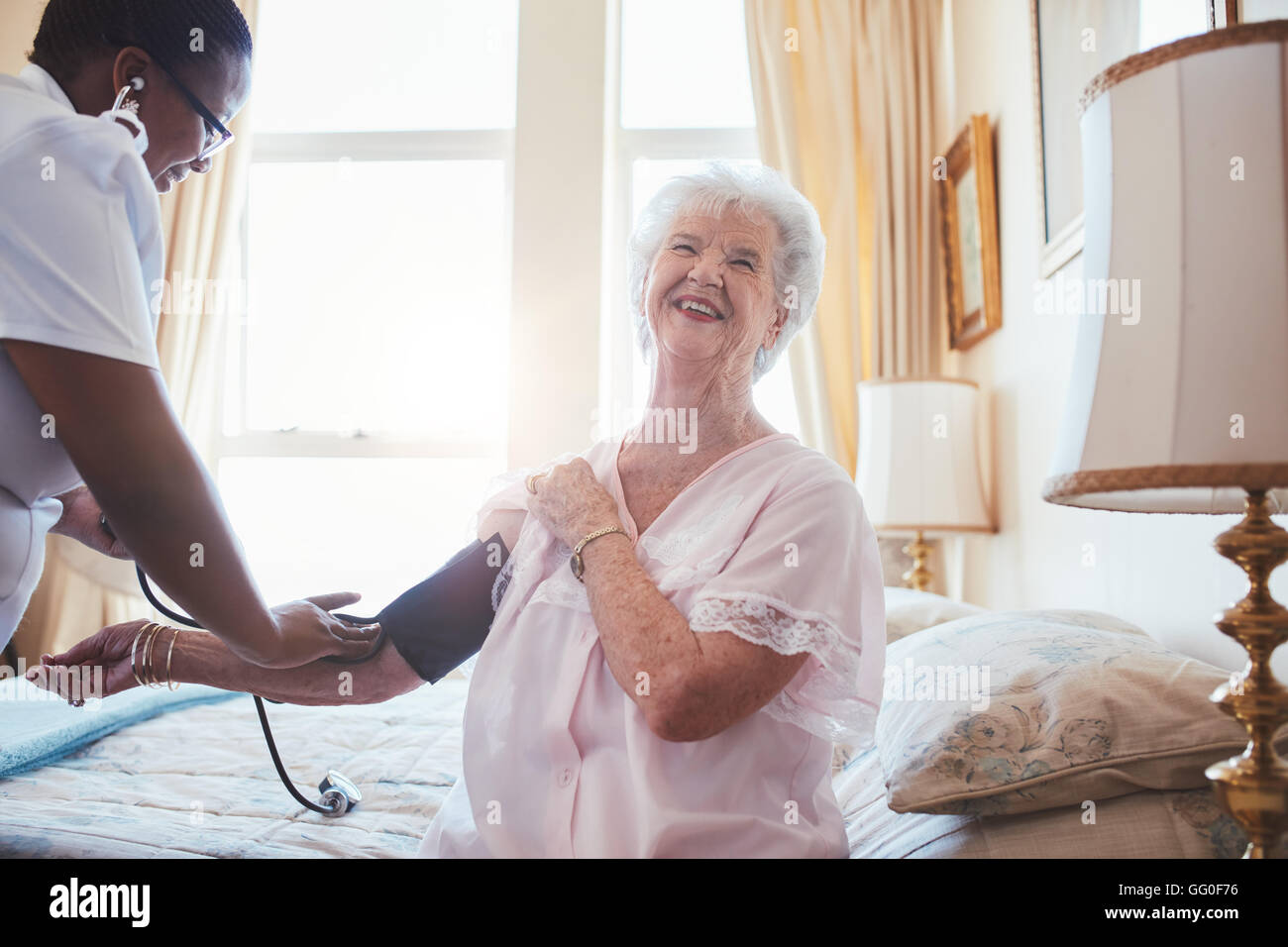 Medico donna la misura della pressione del sangue di donna senior. Donna anziana seduta sul letto e sorridere mentre infermiera controllando il suo sangue Foto Stock