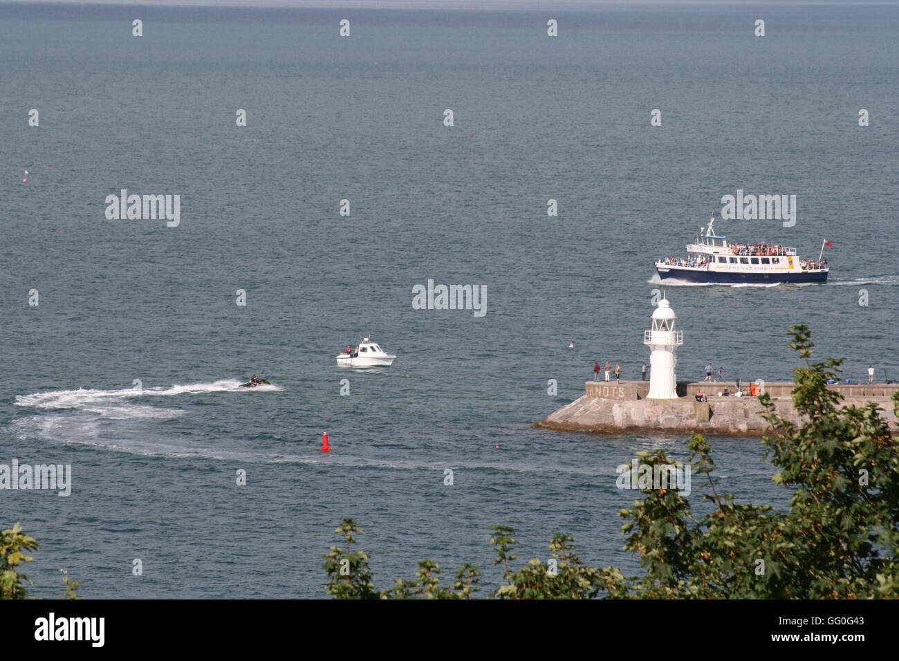 Vista di frangiflutti e il faro con persone di pesca, traghetto, motonautica e jet ski in mare Foto Stock