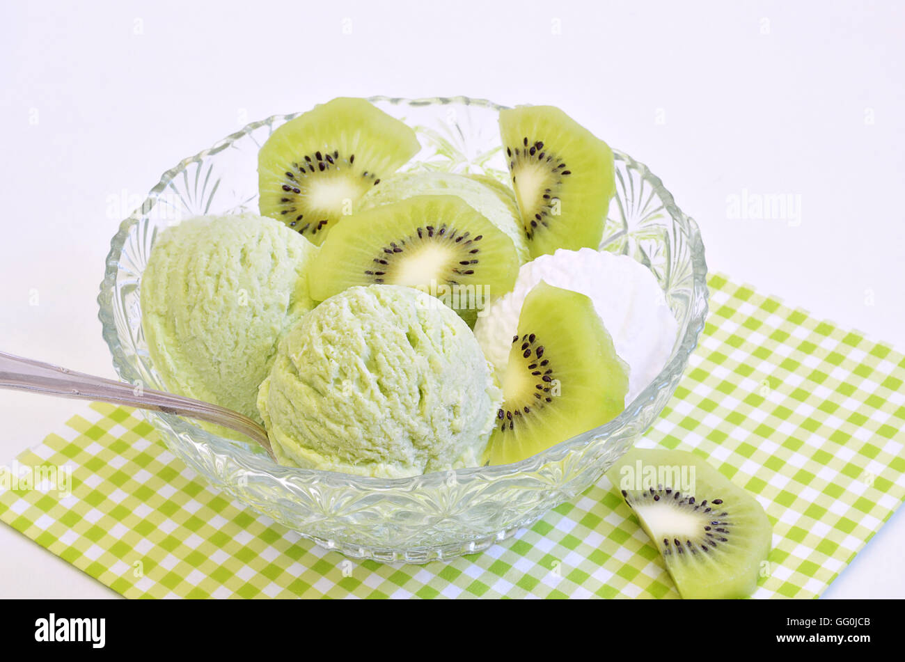 Gelato alla vaniglia e kiwi gelato con fette di kiwi in una ciotola su bianco e la luce verde tovagliolo a scacchi, macro Foto Stock