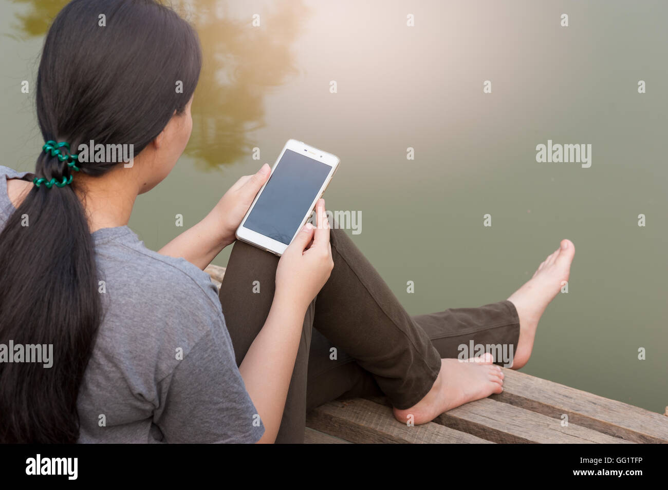 Fine Settimana lifestyle mattina. Giovane donna con il suo telefono cellulare seriamente seduti all'aperto accanto al fiume nella mattina tempo. Foto Stock
