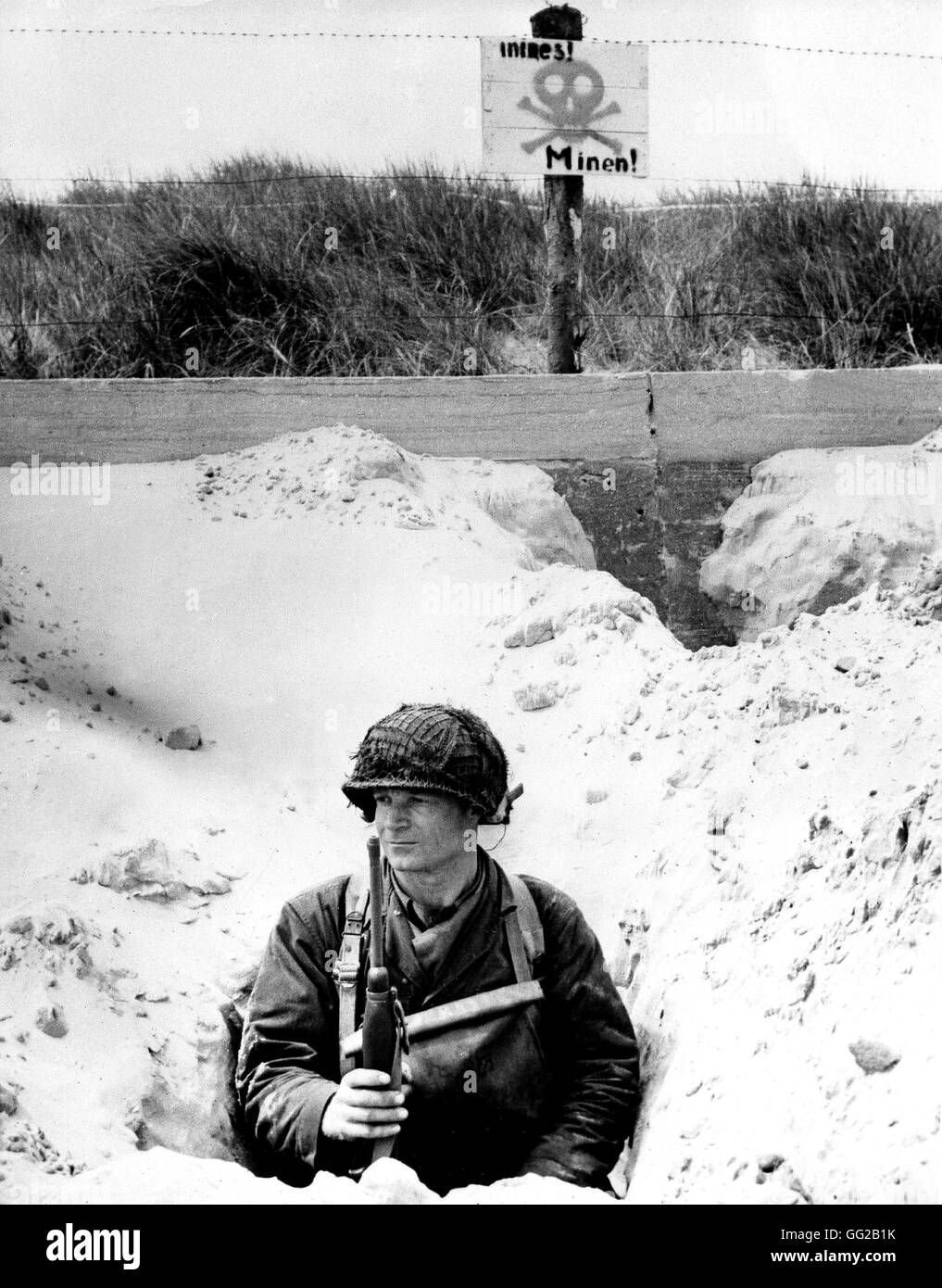 Sbarco in Normandia: un soldato americano nascosto in una trincea orologi la spiaggia al di sopra di lui, la targhetta in tedesco si legge che la zona è minata Giugno 1944 Francia, la seconda guerra mondiale la guerra degli archivi nazionali, Washington Foto Stock