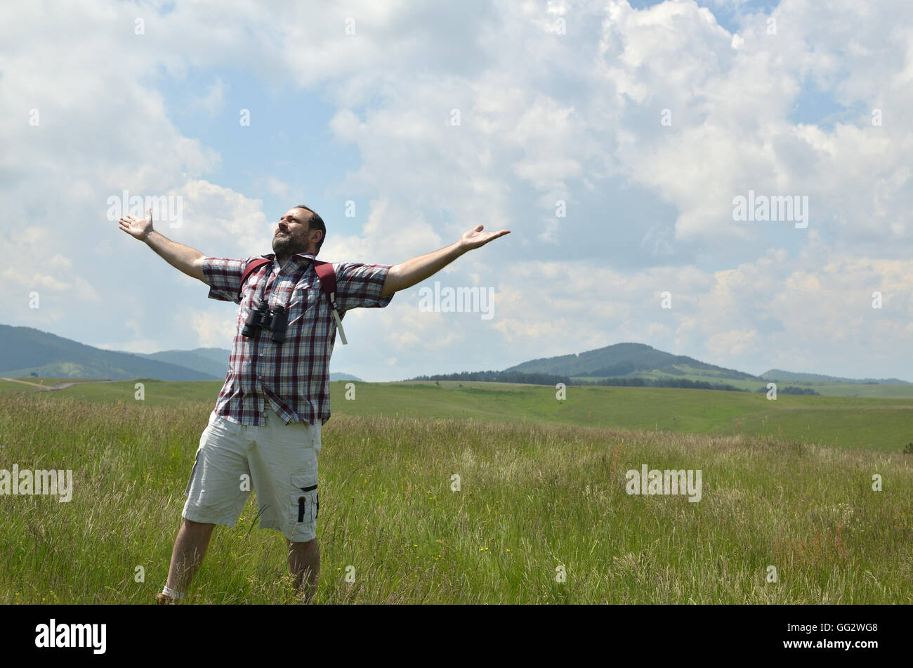 Escursionista con il binocolo ha smesso di camminare su un prato per un po', voltò la faccia verso il sole e diffondere le sue braccia. Colline e nuvoloso Foto Stock