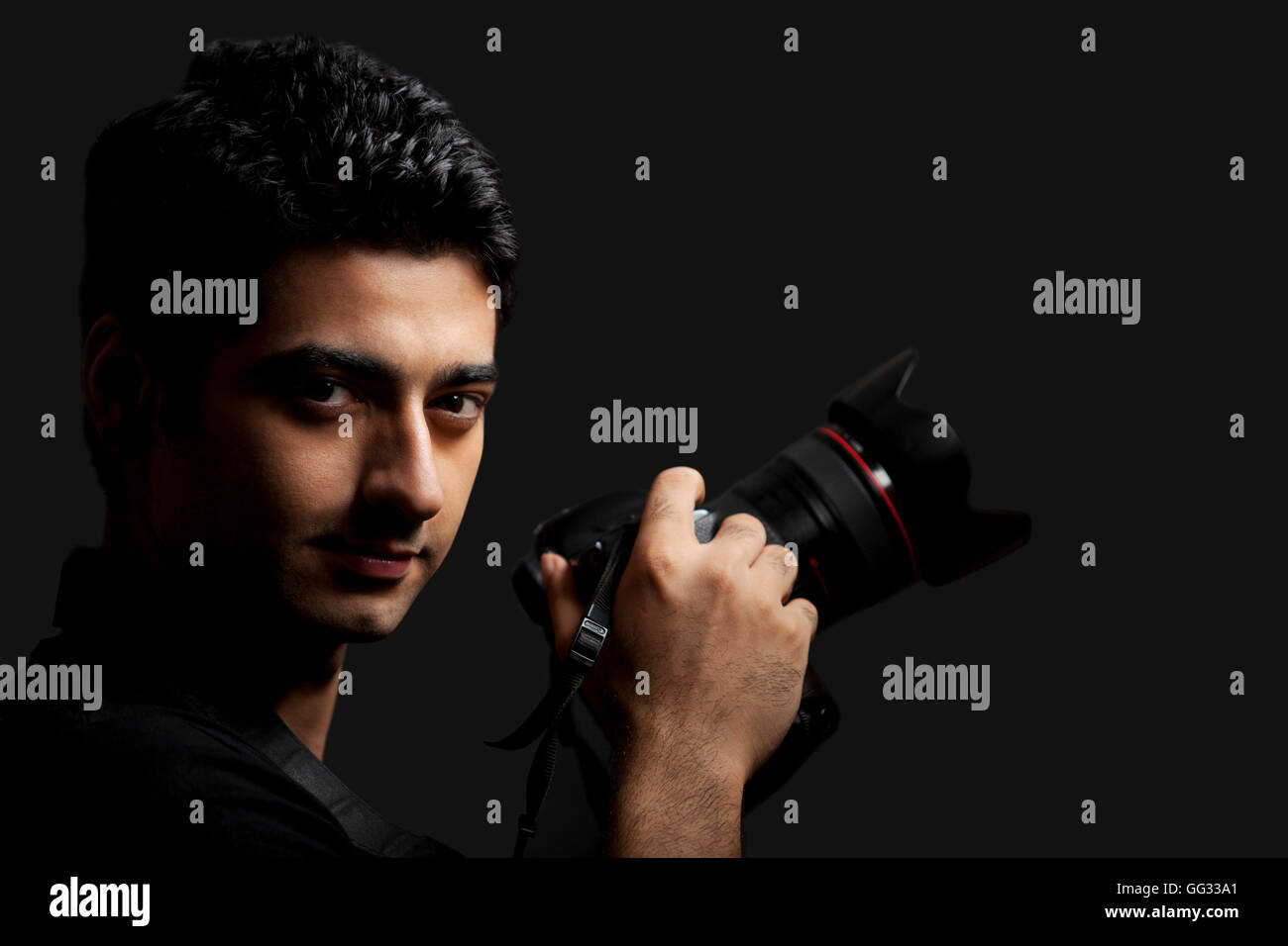 Close-up di giovane maschio fotografo tenere la fotocamera su sfondo nero Foto Stock