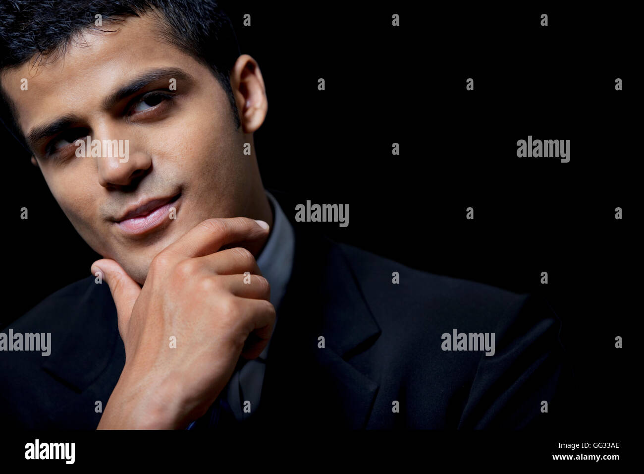 Fiducioso uomo d affari con la mano sul mento su sfondo nero Foto Stock