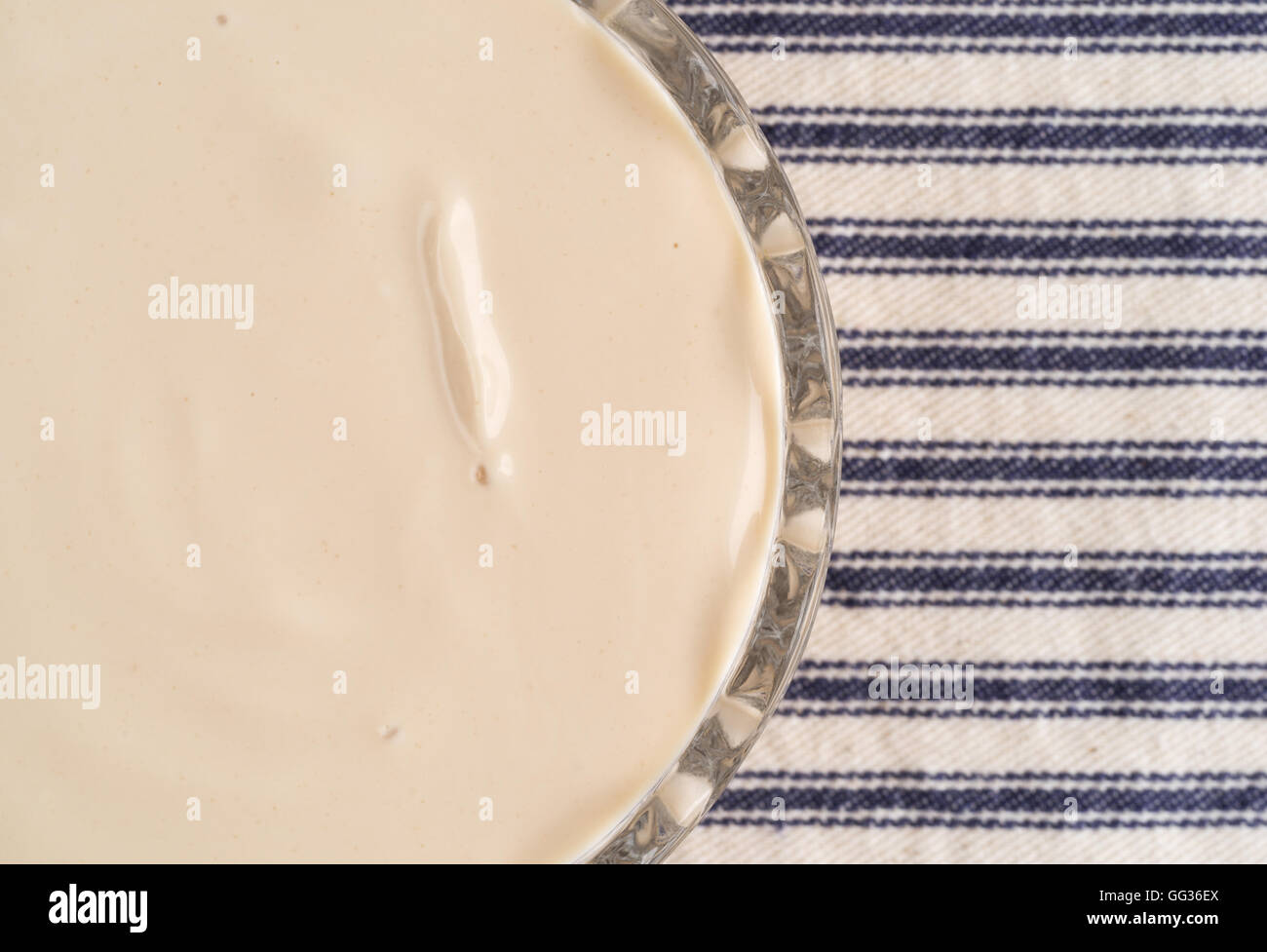 Top vista ravvicinata di una piccola ciotola di vetro di caffè aromatizzati yogurt sulla cima di una tovaglia a righe. Foto Stock