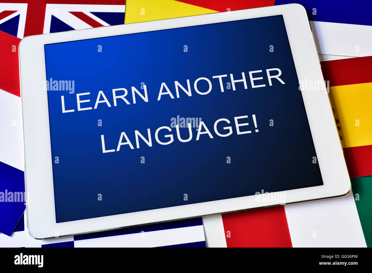 Il testo imparare un'altra lingua sullo schermo di un computer tablet circondato da bandiere di paesi diversi Foto Stock