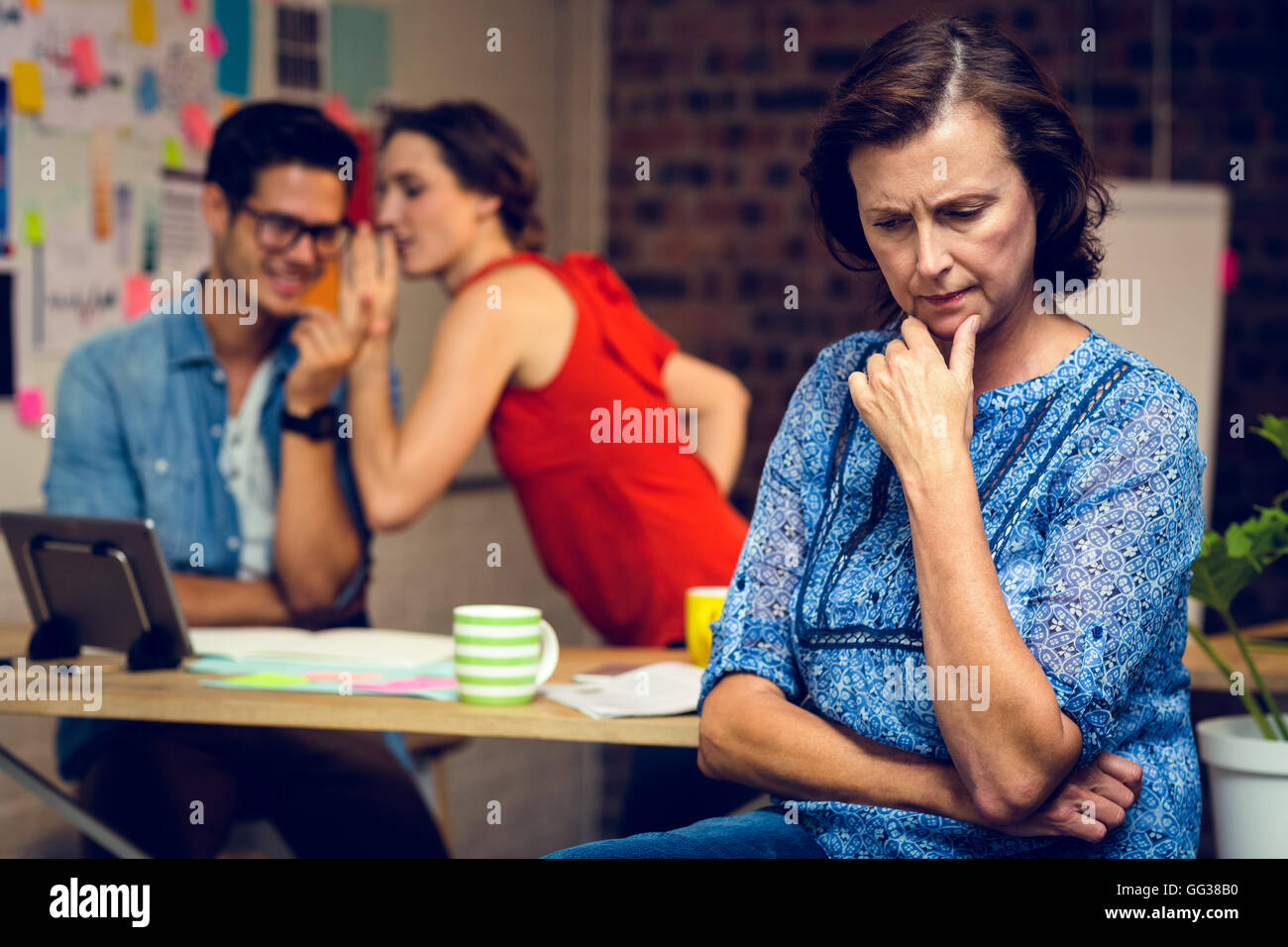 Imprenditrice nel pensiero profondo e colleghi whispering in background Foto Stock