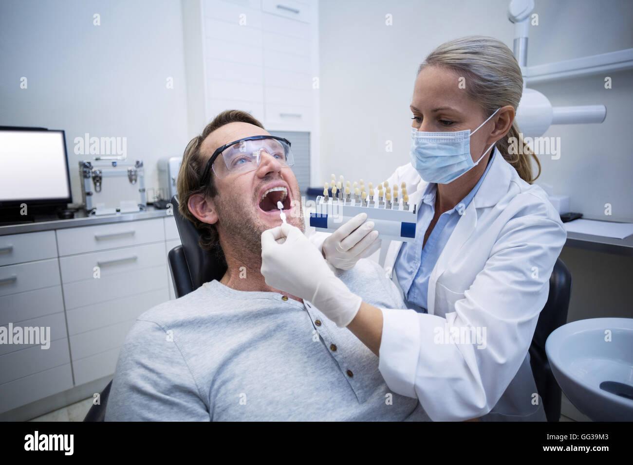 Dentista femmina esame paziente di sesso maschile con sfumature dei denti Foto Stock