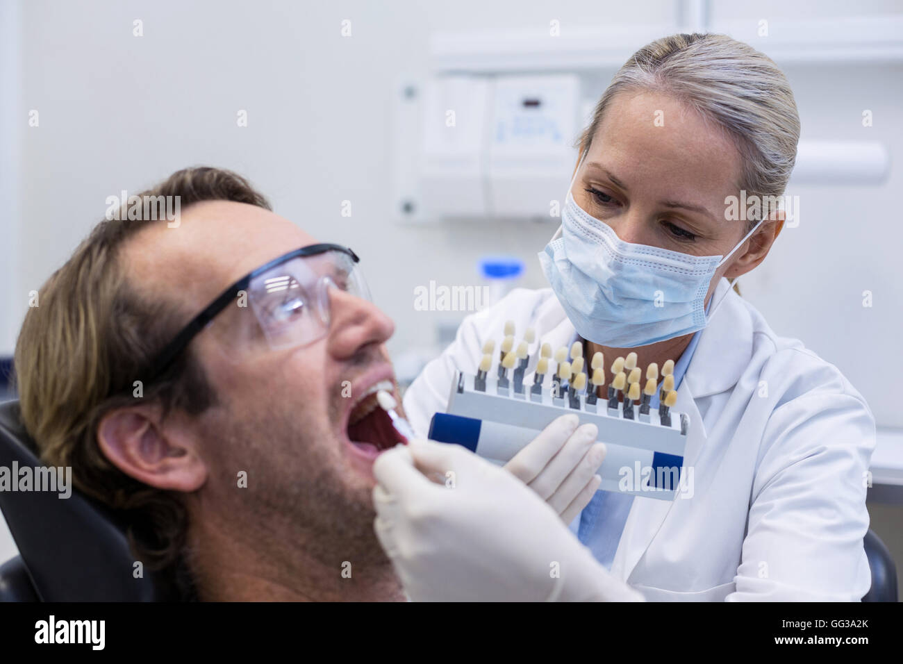 Dentista femmina esame paziente di sesso maschile con sfumature dei denti Foto Stock