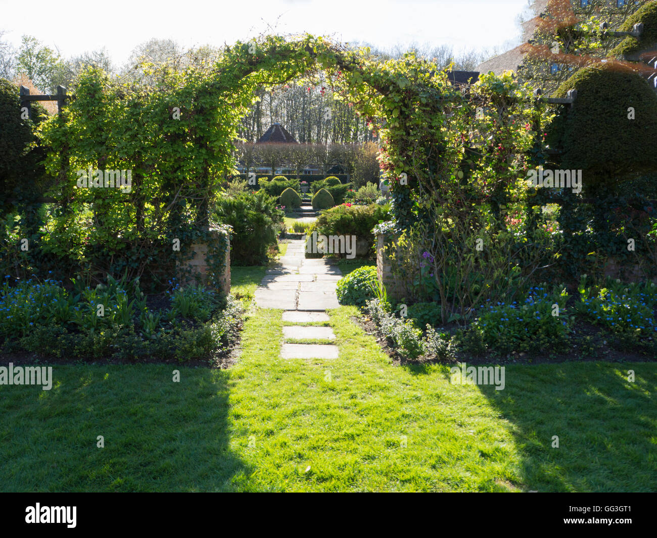 Sole e ombra attraverso il trellis arch con pavimentazione che conduce a Chenies Manor Sunken garden in primavera.Un invitante giardino scena. Foto Stock