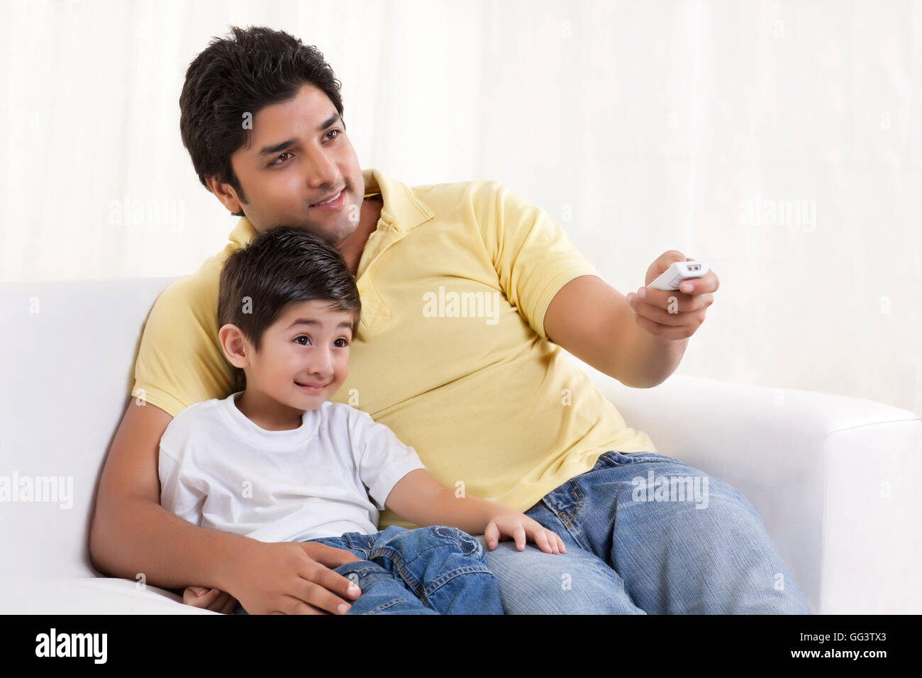 Padre sorridente cambiando canali durante la seduta con suo figlio Foto Stock