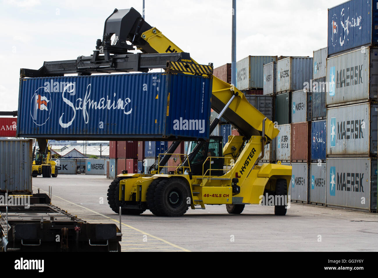 Una pesante macchina di sollevamento di carico e scarico di merci e i contenitori di spedizione su treni merci in una ferrovia porto o scalo merci. Foto Stock