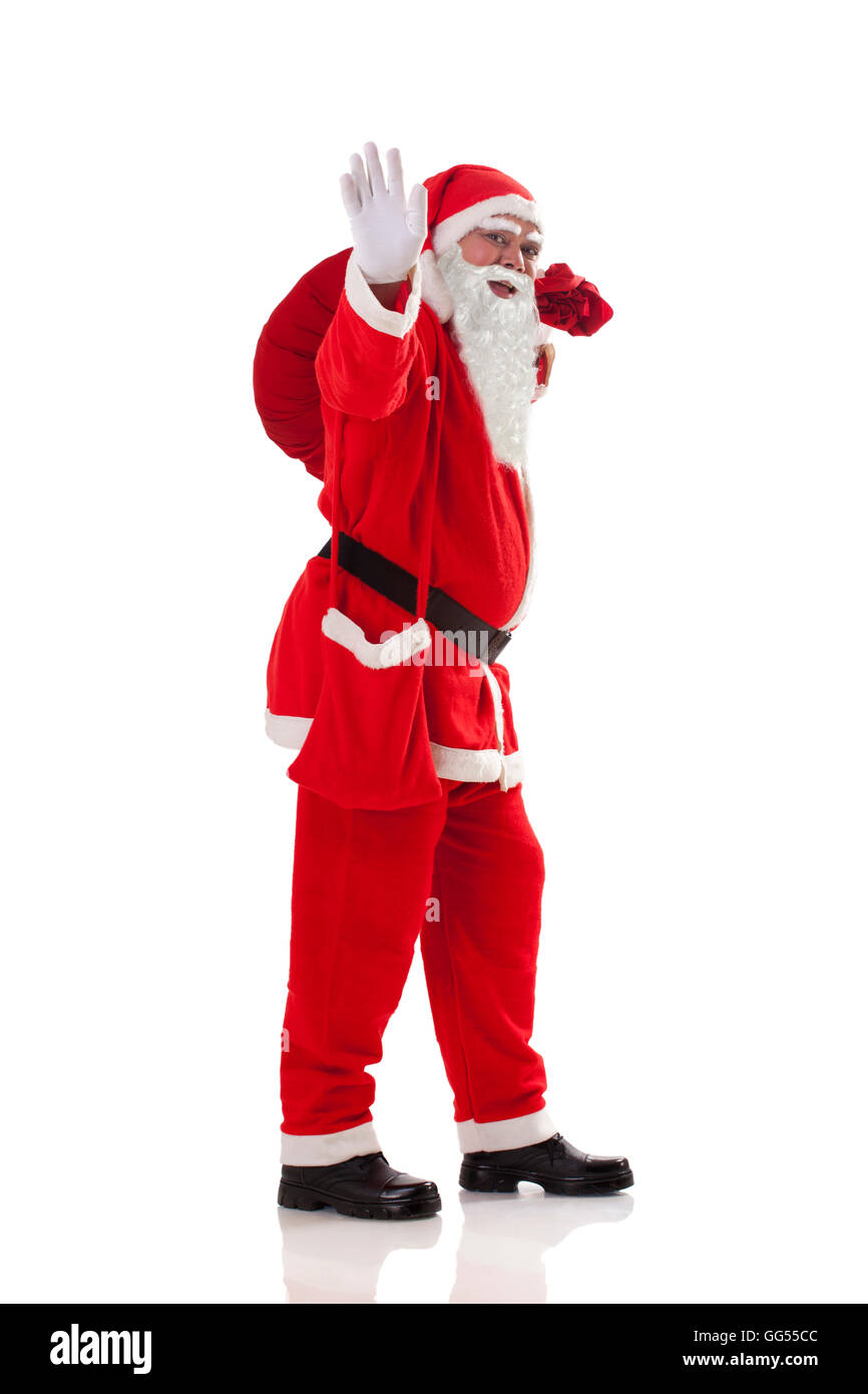 Lunghezza completa di Santa Claus sventolare mentre trasportano il sacco pieno di regali su sfondo bianco Foto Stock