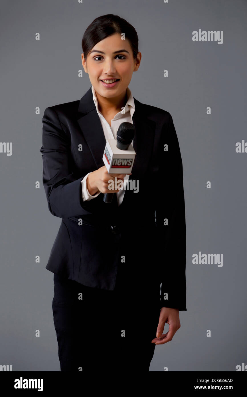 Ritratto di donna news reporter tenendo fuori microfono su sfondo nero Foto Stock