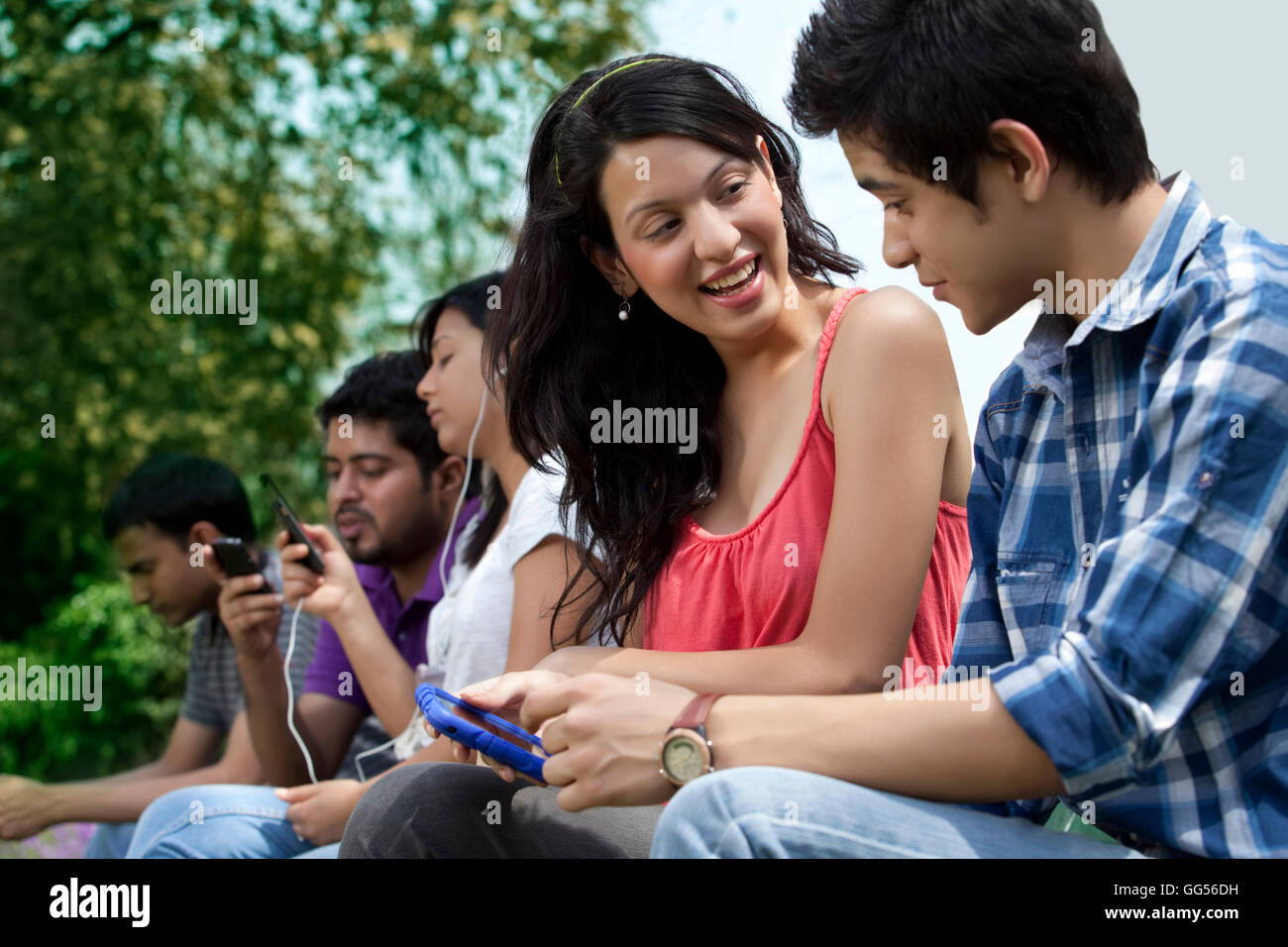 Gli amici utilizzando il telefono cellulare con le persone in background Foto Stock