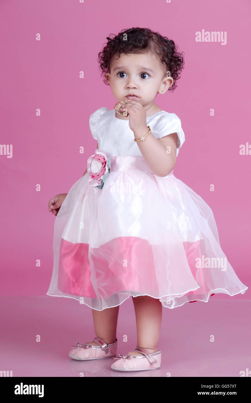 Per tutta la lunghezza della ragazza innocente mangiare cookie contro sfondo rosa Foto Stock