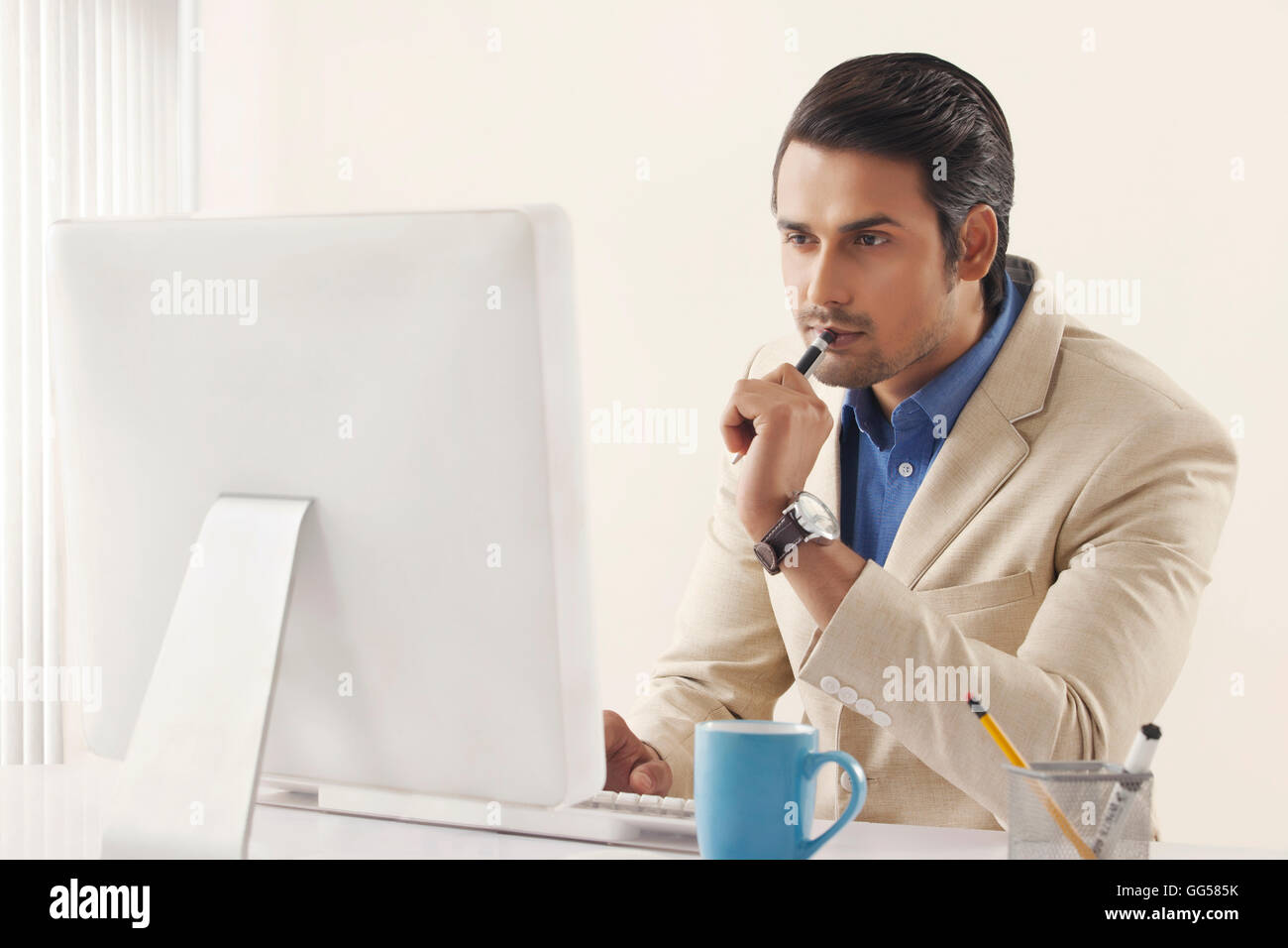 Concentrato giovane imprenditore indiano lavorando sul computer in ufficio Foto Stock