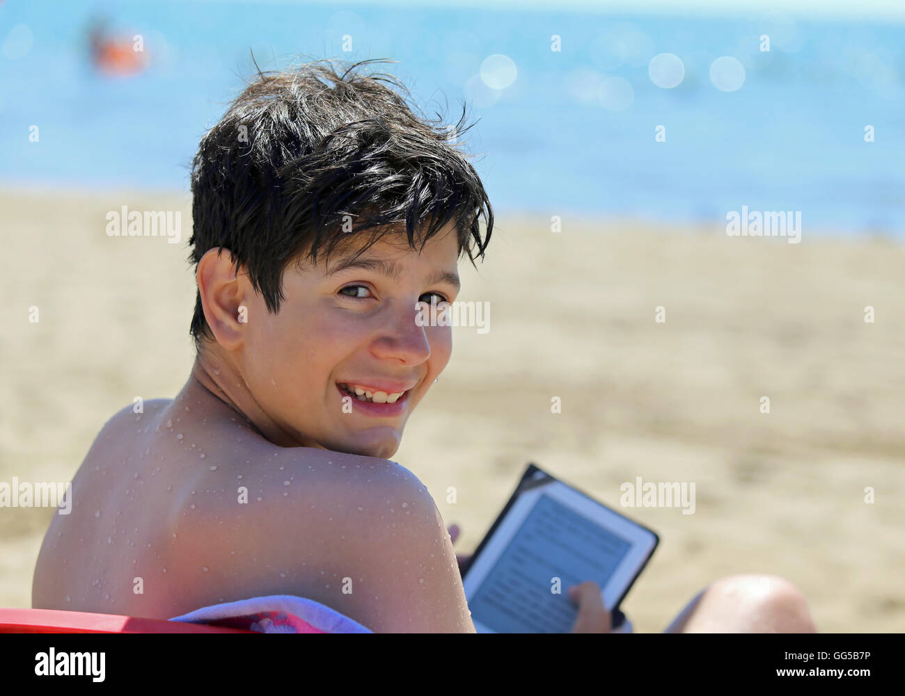 Sorridente giovane ragazzo legge ebook sulla spiaggia in estate Foto Stock