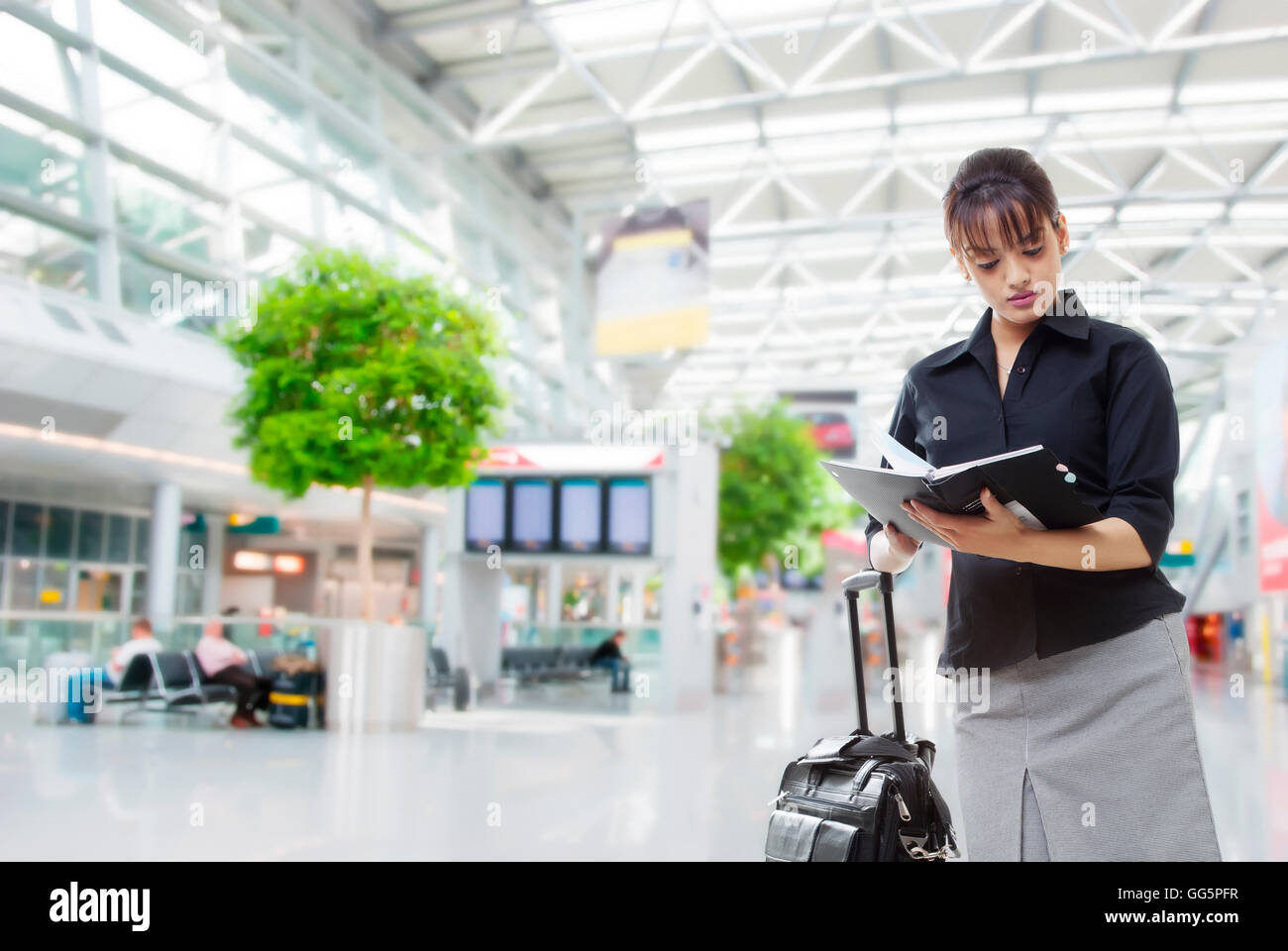 Bella imprenditrice con bagagli libro di lettura in un aeroporto Foto Stock