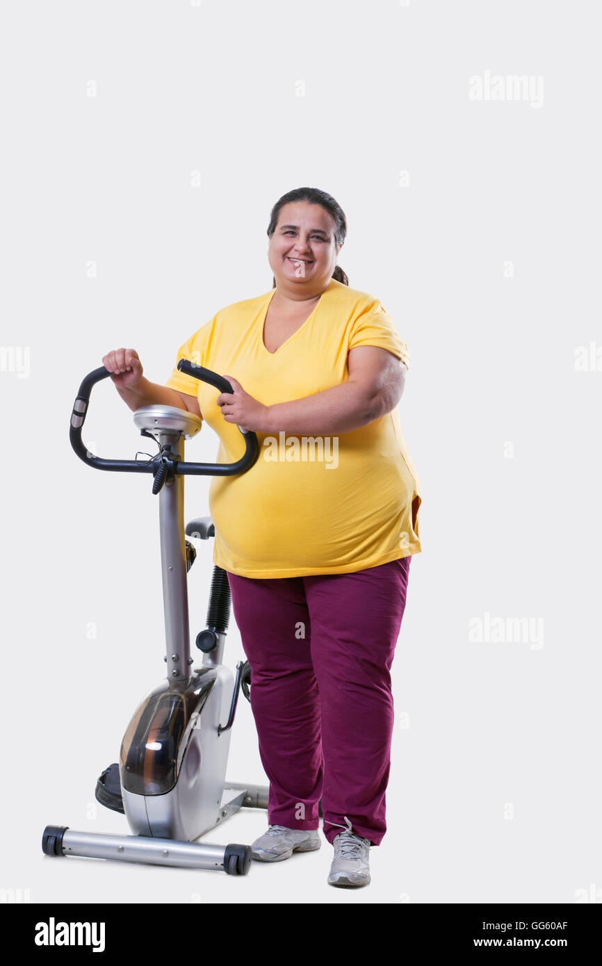 Lunghezza completa di una donna sovrappeso in piedi da una cyclette su sfondo bianco Foto Stock