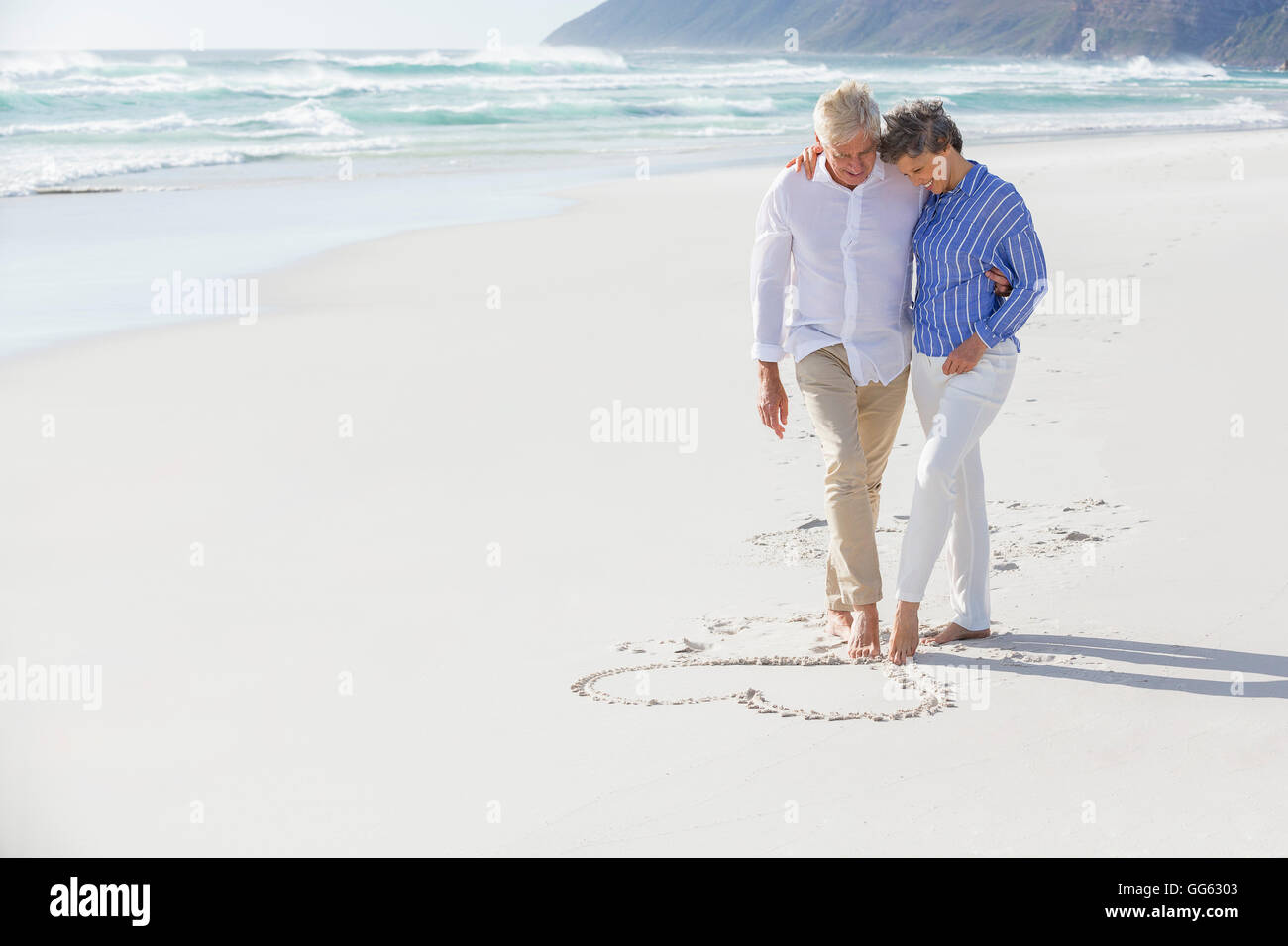 Giovane disegno forma di cuore sulla sabbia con i loro piedi Foto Stock