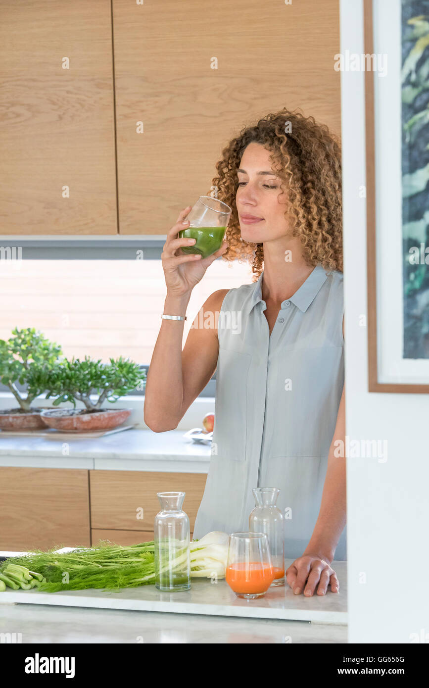 Giovane donna di bere succo di verdura in cucina Foto Stock