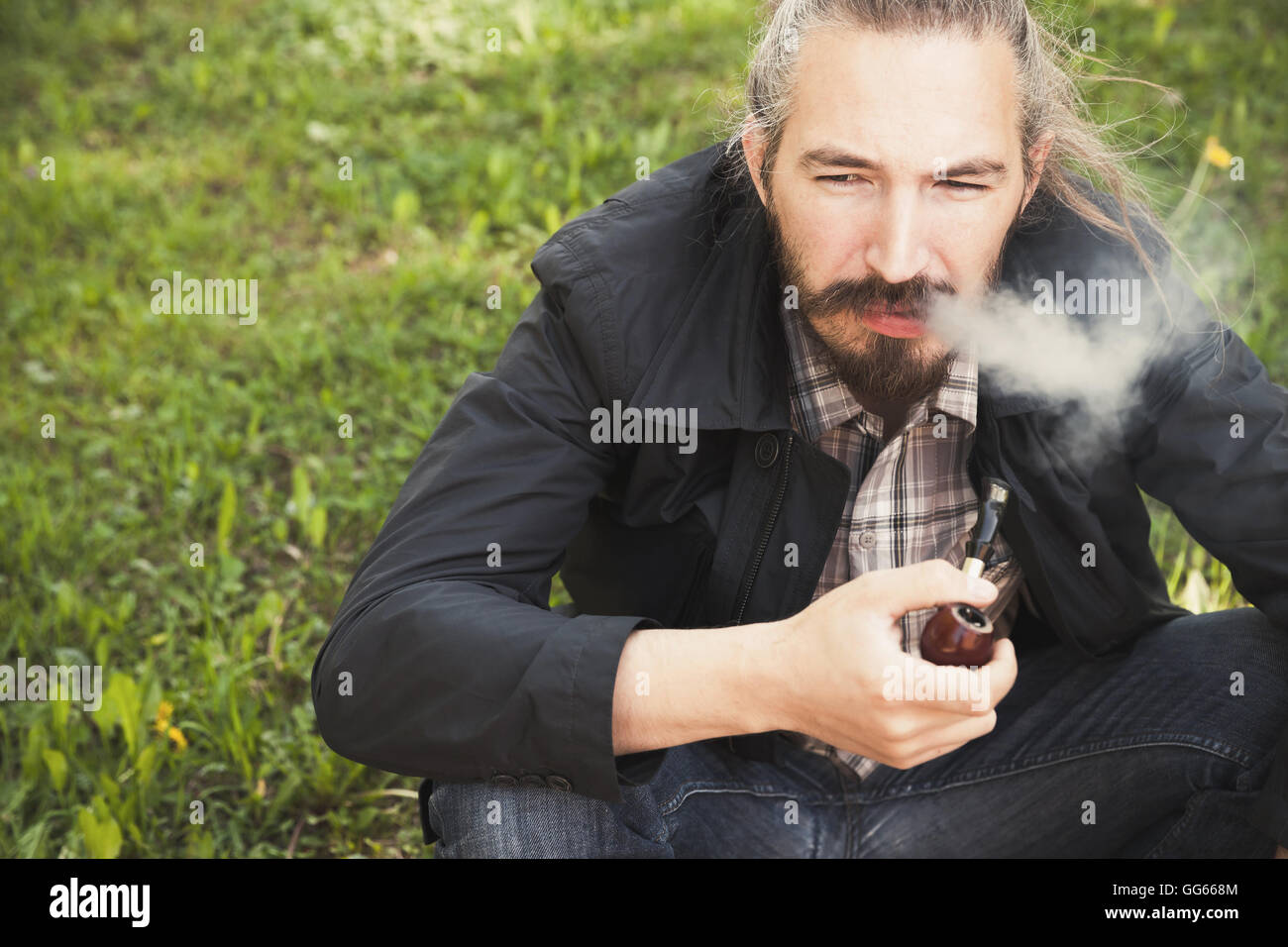 Uomo asiatico fumare una tubazione sull'erba verde nel parco, closeup foto con messa a fuoco selettiva Foto Stock