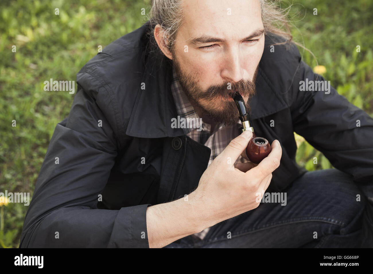 Uomo asiatico fumare una tubazione sull'erba verde nel parco, close-up verticale con il fuoco selettivo Foto Stock