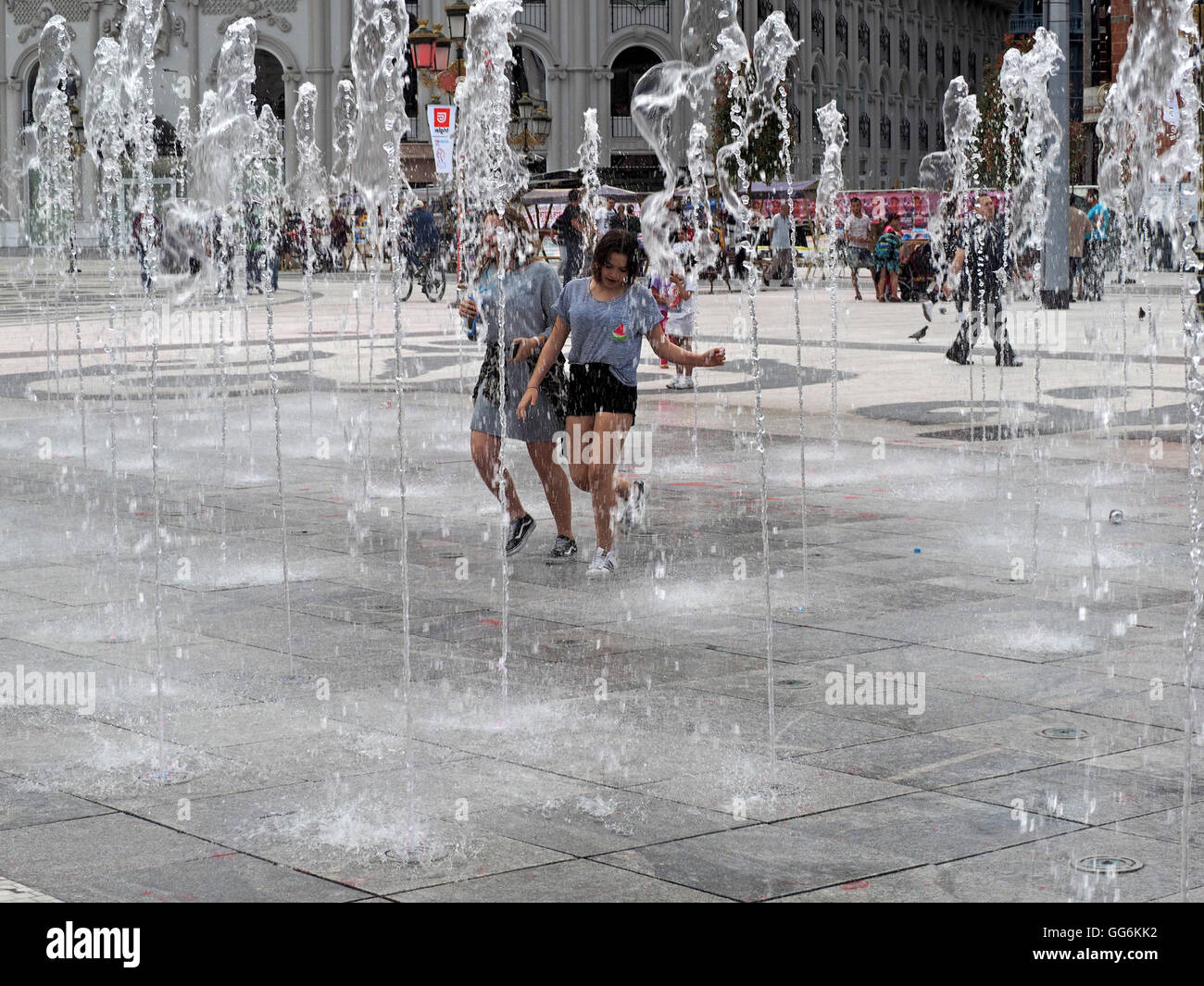 Due giovani donne correre attraverso la pavimentazione di getti di acqua fontana nella piazza Skopje Macedonia Foto Stock
