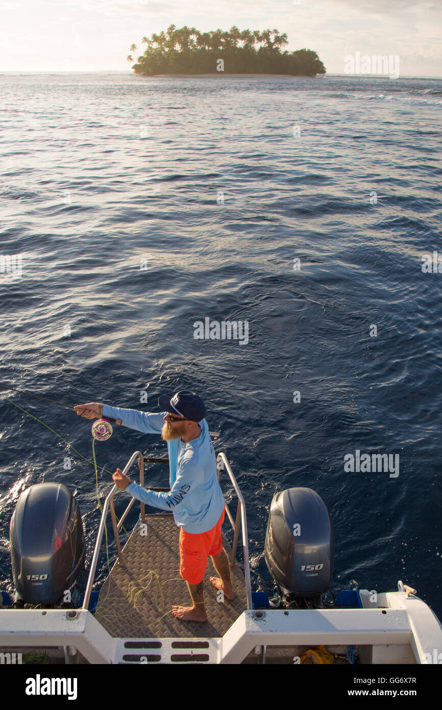 Il pescatore Jonathan Jones getta la sua canna da mosca fuori il retro di una barca mentre la pesca a mosca nei pressi di Samoa all'alba con una piccola isola in background. Foto Stock