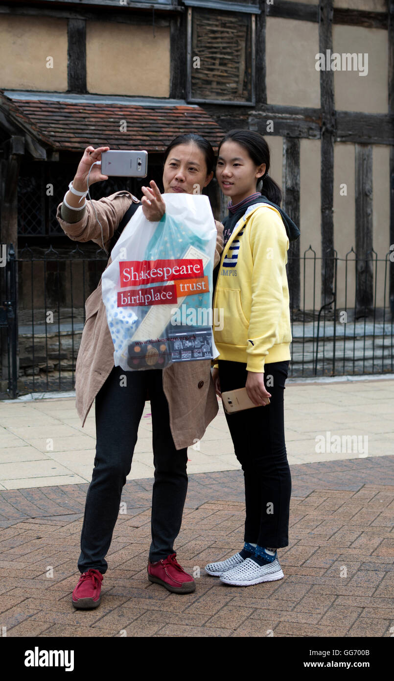 I turisti cinesi tenendo selfie fotografia al di fuori di William al luogo di nascita di Shakespeare, Stratford-upon-Avon, Warwickshire, Regno Unito Foto Stock