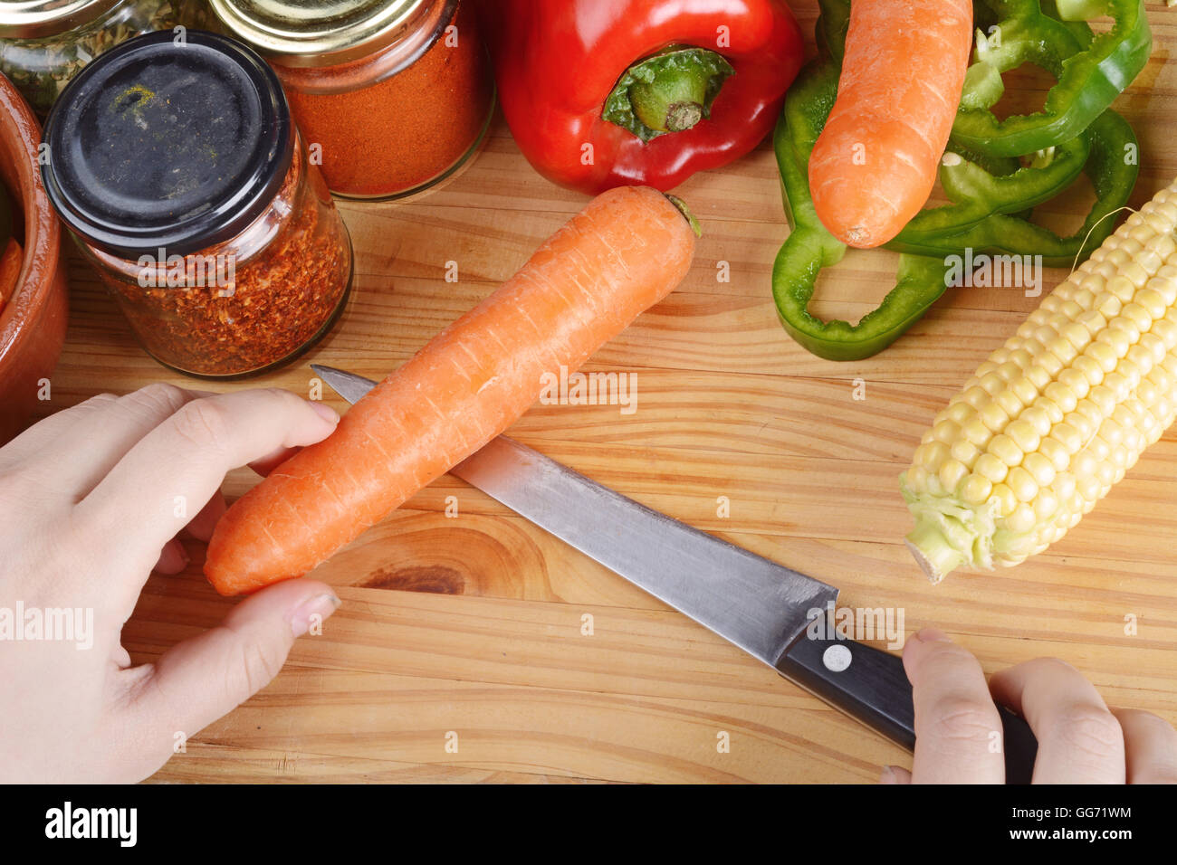 Persona il taglio di una carota sul tavolo di legno con spezie e verdure. Cibo sano concetto. Foto Stock