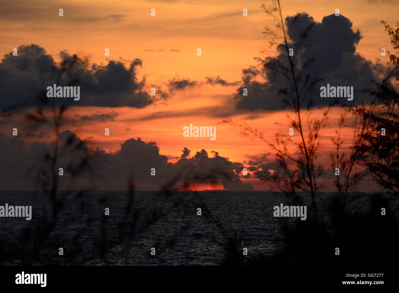 Brillante arancio tramonto con nuvole nere su una spiaggia tropicale Foto Stock