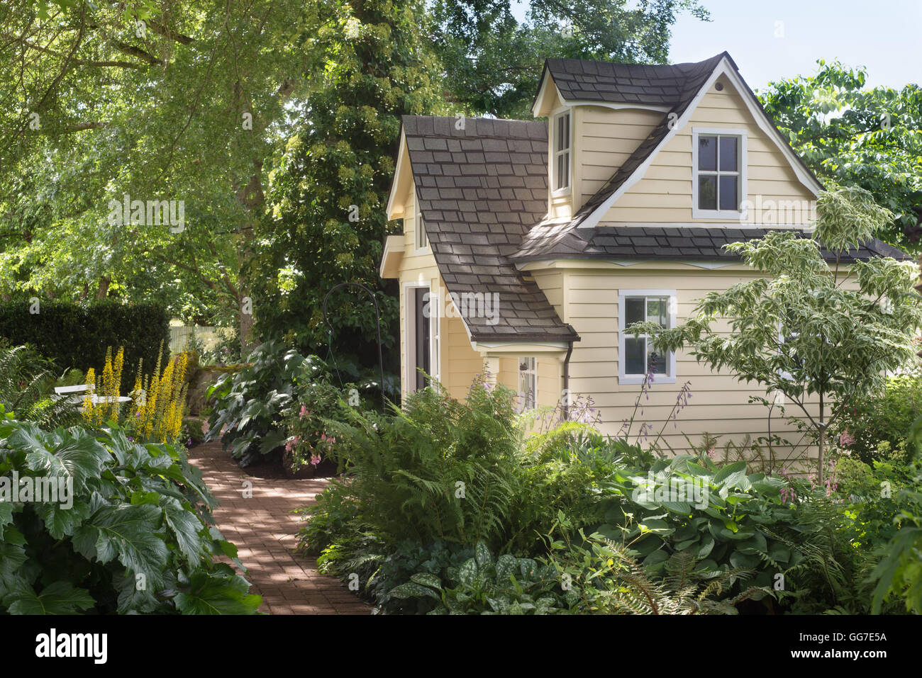 Un affascinante playhouse cottage si trova in un ombreggiato giardino perenni. Foto Stock