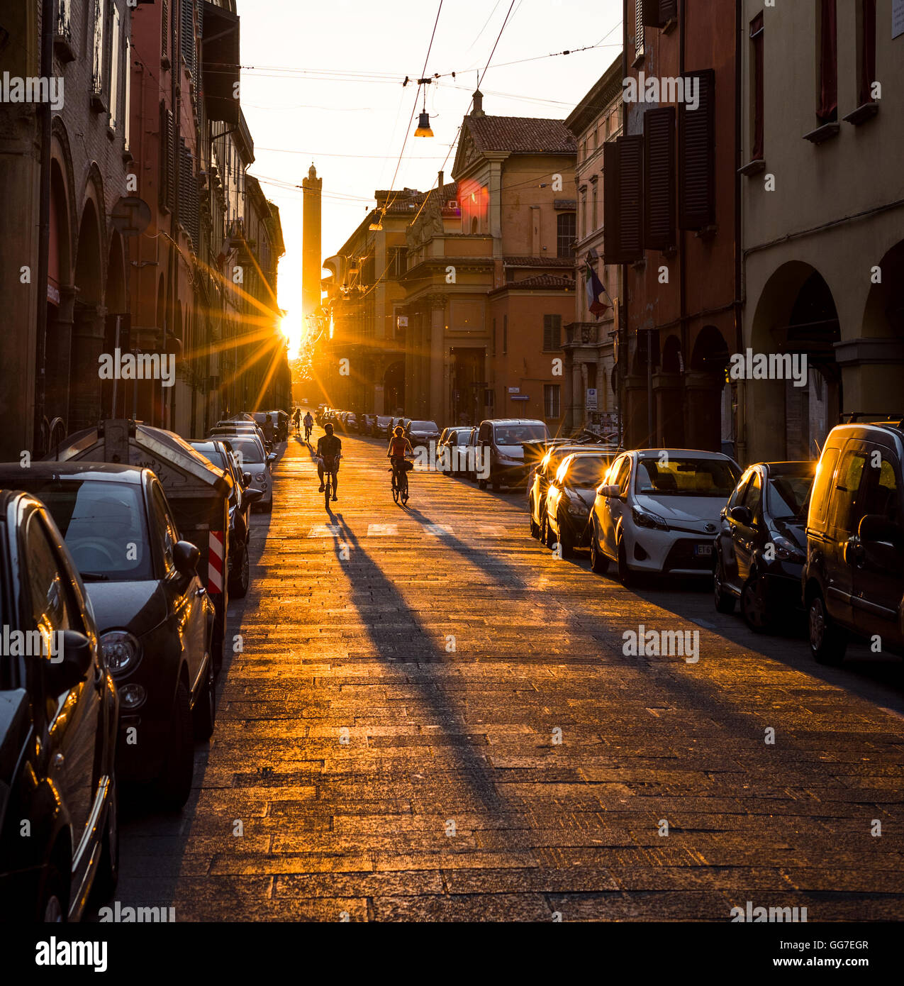 I ciclisti attraversamento strada Maggiore di Bologna al tramonto con la Torre degli Asinelli torre in background. Emilia Romagna. L'Italia. Foto Stock