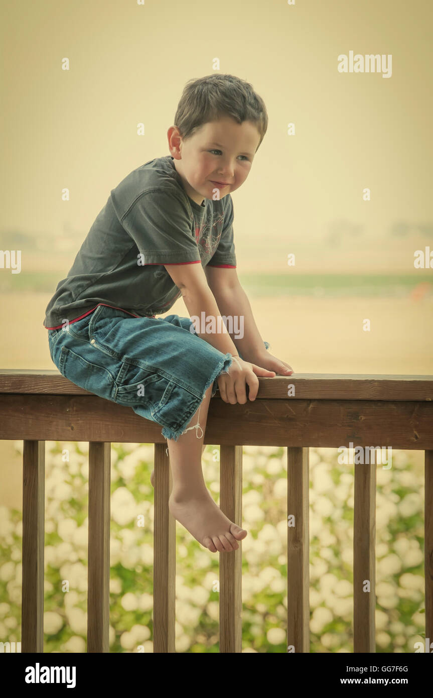 Carino piccolo ragazzo seduto sul portico sul retro della ringhiera mentre godendo la sua estate. Retrò instagram look. Foto Stock