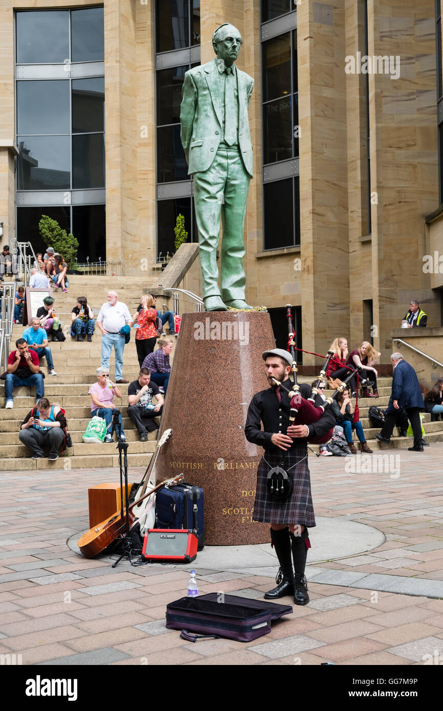 La gente seduta fuori nel sole sulle fasi di Glasgow Royal Concert Hall suonatore ambulante con riproduzione di cornamuse a Glasgow, Scozia, unità Foto Stock