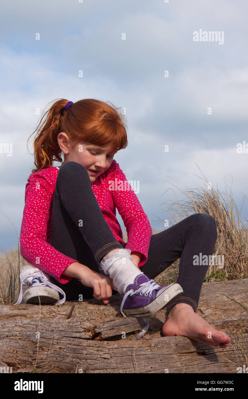 Poco i Capelli rossi ragazza di vincolare il suo lacci delle scarpe su viola sneakers Foto Stock